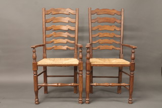 A pair of elm ladder back carver chairs with woven rush seats, raised on turned supports