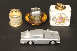 A lighter contained in an Aston Martin shaped pottery case, a  lighter contained in a Continental porcelain case and 2 other table  lighters