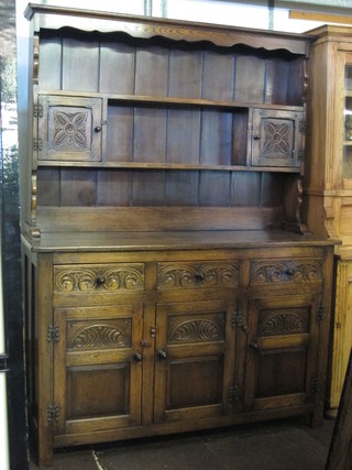A carved oak dresser the raised back fitted 2 shelves and 2 cupboards, the base fitted 3 drawers above a triple cupboard 55"