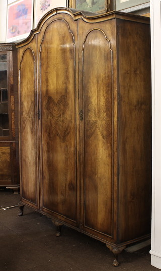 A Queen Anne style arch shaped walnut triple wardrobe with  moulded cornice, raised on cabriole supports 63"