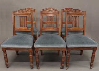 A set of 6 Edwardian carved oak stick and bar back dining chairs  with upholstered seats, raised on turned supports