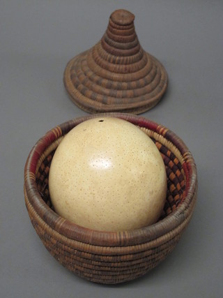 A circular Eastern basketware jar and cover containing an ostrich egg