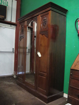 A Victorian carved mahogany triple wardrobe with moulded and  dentil cornice, the centre fitted arched bevelled plate mirror  panelled door, flanked by a pair of cupboards enclosed by  panelled doors, raised on a platform base 60"