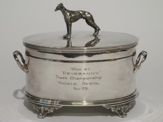 An oval silver plated twin handled caddy/racing trophy, the finial  in the form of a standing greyhound, marked Won By Deveranny  Track Champion Knowle Bristol November 1936,   ILLUSTRATED
