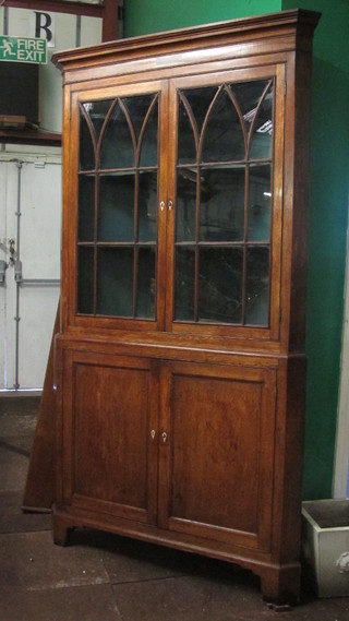 A Georgian Country oak double corner cabinet the upper section  with moulded cornice, the shelved interior enclosed by astragal  glazed panelled doors, the base fitted a double cupboard enclosed  by panelled doors with ivory escutcheons, raised on bracket feet  49"