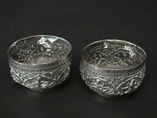 A pair of circular Eastern embossed white metal bowls decorated figures of seated Deities