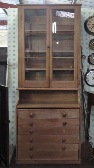 A 19th Century Continental stripped pine bookcase on chest, the  upper section with adjustable shelves enclosed by glazed panelled  doors, above a recess, the base fitted 4 long drawers, raised on a  platform base 34"