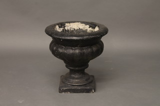 A circular black painted garden urn with lobed body, raised on a square base 17"