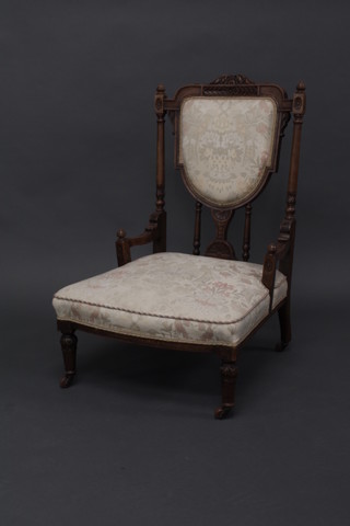 A Victorian carved walnut show frame nursing chair with upholstered seat and back, raised on turned supports