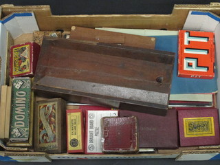 A wooden box with sliding lid containing a collection of playing cards and a collection of dominoes, board games etc