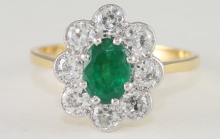 An 18ct yellow gold dress ring set an oval cut emerald  surrounded by diamonds, approx 0.80/0.80ct