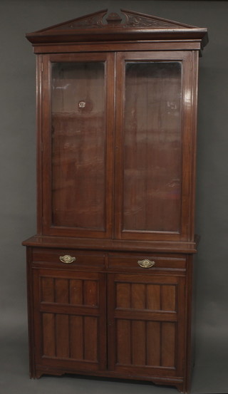 An Edwardian walnut display cabinet on cabinet, the upper section with broken pediment, the interior fitted adjustable  shelves enclosed by glazed panelled doors, the base fitted 2 long  drawers above a double cupboard, raised on a platform base 41"