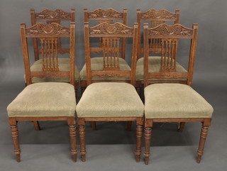A set of 6 Edwardian carved oak stick and rail back dining chairs with upholstered seats, raised on turned supports