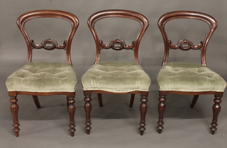 A set of 3 Victorian mahogany balloon back dining chairs with carved mid rails and upholstered seats, raised on turned supports