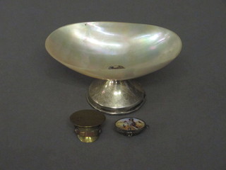 A mother of pearl scallop shaped salt raised on a silver spreading  foot, an Egyptian gilt metal locket in the form of a Moses basket  with enamelled hinged lid and a miniature Trench art model of a  cap