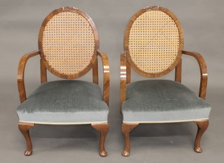 A pair of 1940's walnut open arm chairs with woven cane backs  and upholstered seats, raised on cabriole supports