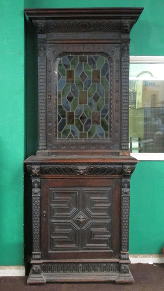 A Victorian heavily carved oak cabinet on cabinet, the upper section with moulded cornice, fitted shelves enclosed by green  glass panelled doors, the base fitted 1 drawer above a cupboard  enclosed by a panelled door 36"