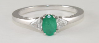 A lady's 18ct white gold dress ring set an oval cut emerald  and with diamonds to each shoulder