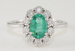An 18ct white gold dress ring set an emerald surrounded by  diamonds