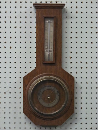 An aneroid barometer and thermometer with silvered dial, contained in an stylised oak wheel case
