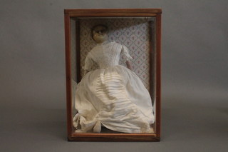 A 19th Century waxed face doll, standing and fully clothed in a display cabinet 17"