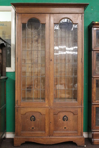 An Art Nouveau inlaid oak bookcase with moulded cornice, the interior fitted adjustable shelves enclosed by lead glazed panelled  doors, the base fitted a cupboard enclosed by inlaid doors, raised  on bracket feet 40"