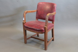 A pair of oak open arm office chairs upholstered in red rexine,  raised on square tapering supports with H framed stretcher