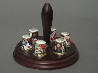A collection of 6 Royal Crown Derby thimbles, raised on a  turned wooden stand