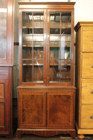 A Georgian style inlaid mahogany display cabinet on cabinet, the  upper section with moulded cornice, the shelved interior enclosed  by astragal glazed panelled doors, the base fitted a cupboard  enclosed by a panelled door, raised on bracket feet 27"