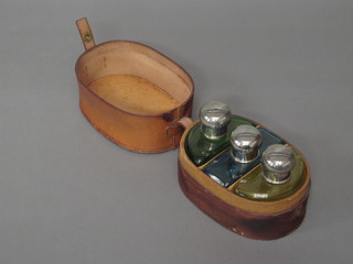 An Art Deco oval leather box fitted 3 coloured glass scent bottles with plated tops