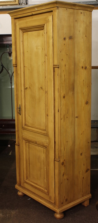 A Continental stripped and polished pine cupboard with moulded cornice and shelved interior enclosed by a panelled door, raised  on bun feet 27"