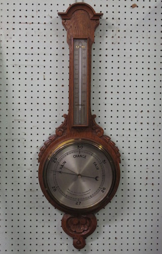An aneroid barometer and thermometer with silvered dial  contained in a carved oak wheel case