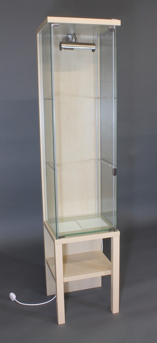 A rectangular glass and light wood display cabinet, raised on square supports 16"