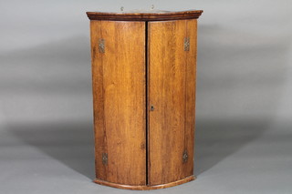 A Georgian oak bow front hanging corner cabinet with shelved  interior enclosed by panelled doors, 23"