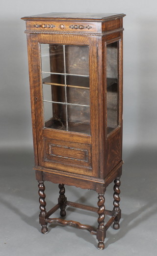 An Art Deco oak display cabinet enclosed by lead glazed  panelled doors, raised on spiral turned and block supports