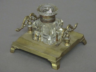 A Victorian square glass inkwell raised on a brass stand incorporating a pen rest, raised on bracket feet 5"