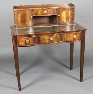 A Georgian style mahogany writing table of serpentine outline, with inset tooled leather writing surface and raised super  structure to the back fitted a drawer above a recess flanked by a  pair of cupboards, the base fitted 1 long and 2 short drawers,  raised on square tapering supports 37"