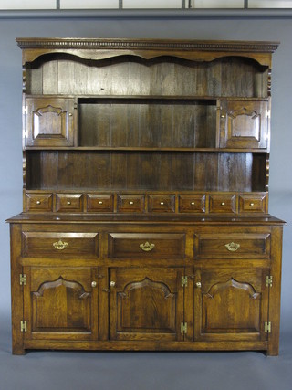 An oak dresser, the raised back with moulded cornice fitted 3 shelves flanked by a pair of cupboards, the base fitted 8 spice  drawers above 3 long drawers with triple cupboard with swan  neck drop handles 66"