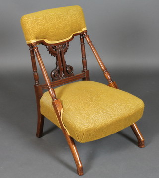 An Edwardian carved walnut nursing chair upholstered in yellow material and raised on turned supports