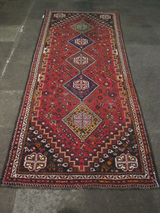 A contemporary red ground rug with 5 diamonds to the centre, some wear 133" x 47"