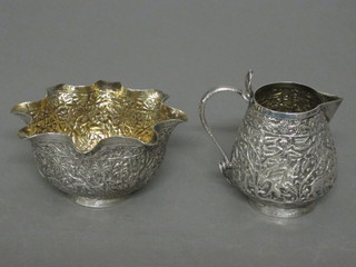 An Indian embossed white metal cream jug with sparrow beak  together with a circular sugar bowl