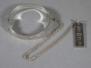 An engraved silver bangle together with a silver ingot pendant hung on a fine chain