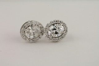 A pair of oval diamond set earrings with diamond surround
