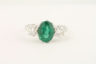 An 18ct white gold dress ring set an oval cut emerald supported  by 2 diamonds, approx. 1.70/0.85ct