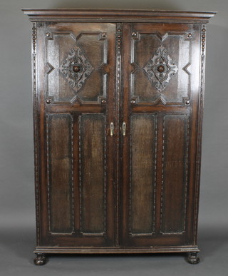 A carved oak Jacobean style wardrobe with moulded cornice, enclosed by panelled doors, raised on bun feet 52"