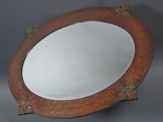 An oval bevelled plate wall mirror contained in an oak and brass mounted frame 33" x 25"