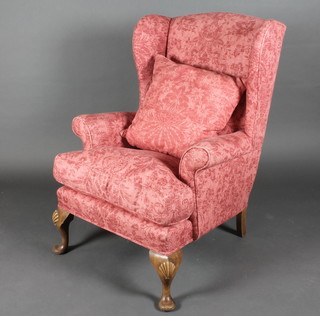 A winged armchair upholstered in red material, raised on cabriole  supports