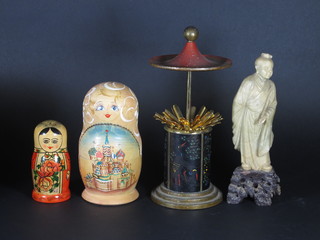 A circular metal cigarette dispenser in the form of a pagoda 5", a  carved soap stone figure 10" and 2 Russian nesting dolls