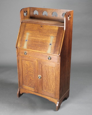A student's Art Nouveau oak bureau with pierced three-quarter  gallery, the fall front revealing a well fitted interior above 1 long  drawer above a cupboard enclosed by panelled doors 25"w x  14"d x 48"h