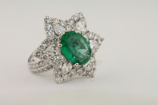 A lady's 18ct white gold star shaped cluster dress ring set an oval cut emerald supported by diamonds